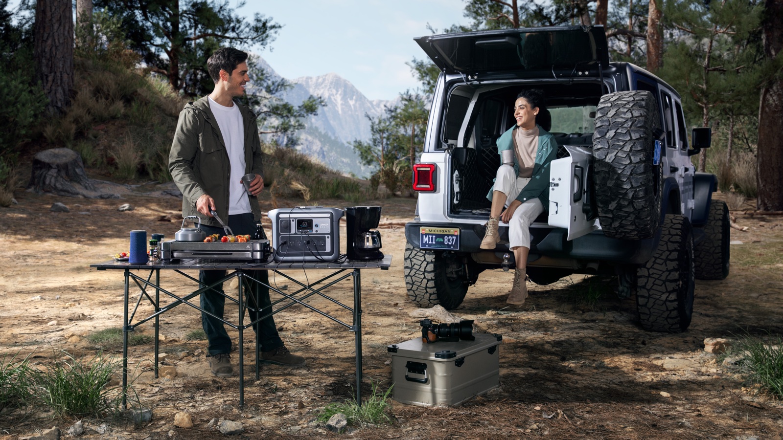 Couple cooking at a folding table beside an off-road vehicle