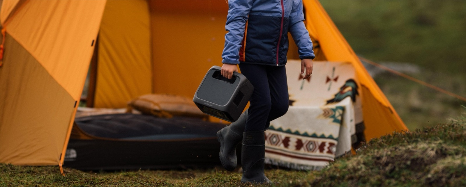 Camper carrying a power station past an open tent